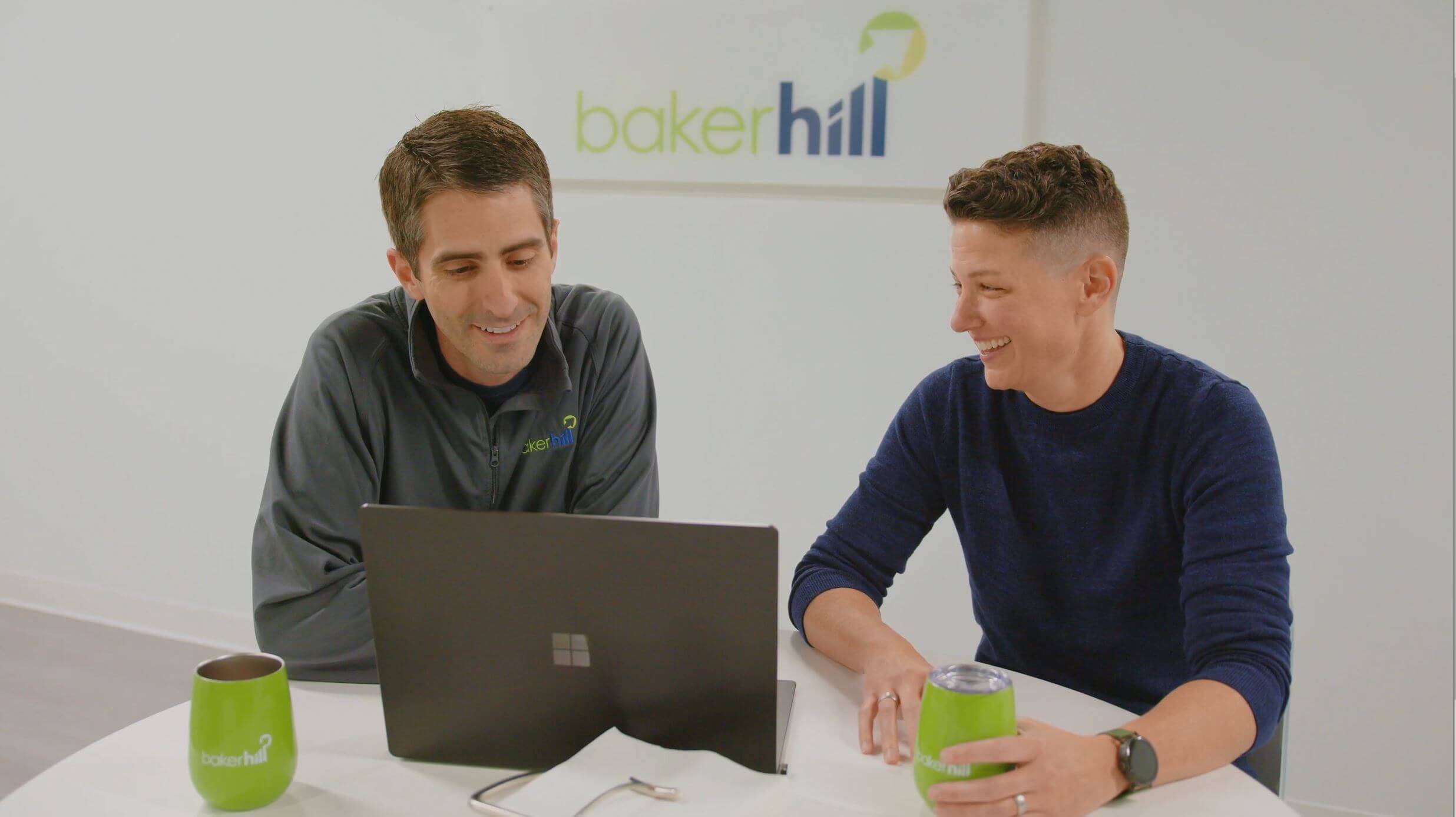 Two Baker Hill employees working together with a laptop at a table.